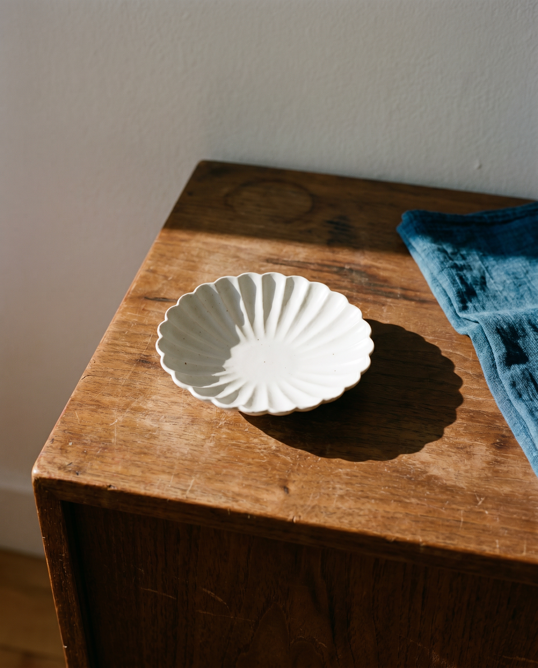 Flower plate set by Mujagi, the three plates clustered at the corner of an oak dining table at rest