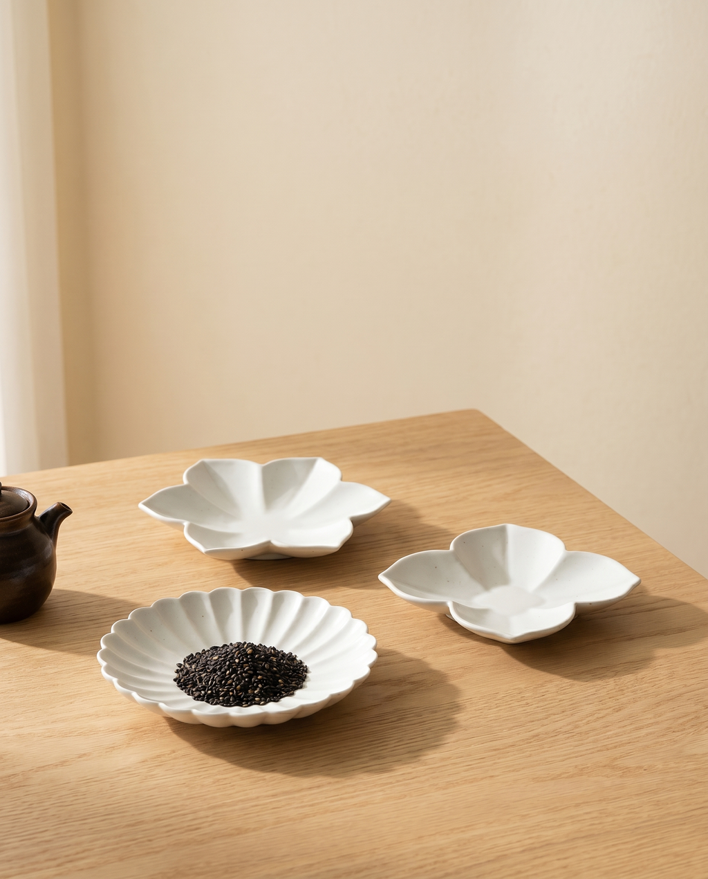 Flower plate set by Mujagi, the three plates clustered at the corner of an oak dining table at rest