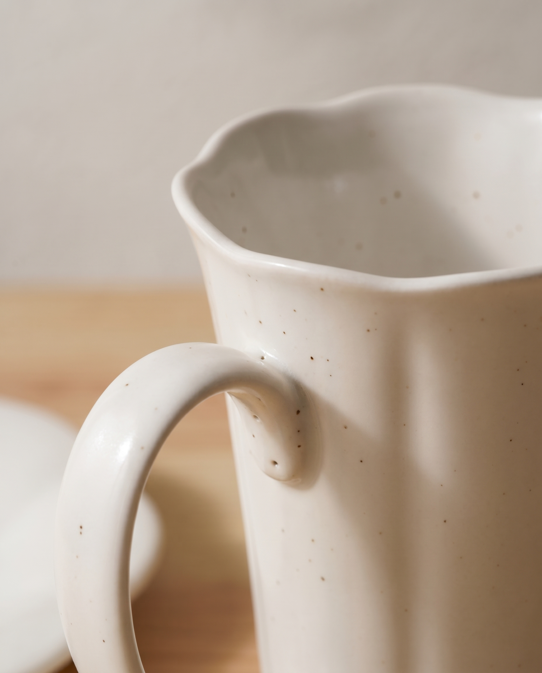 Blooming mug and plate set by Insoil — close-up of a mug rim, scalloped petal-curves and iron-oxide dots in the glaze