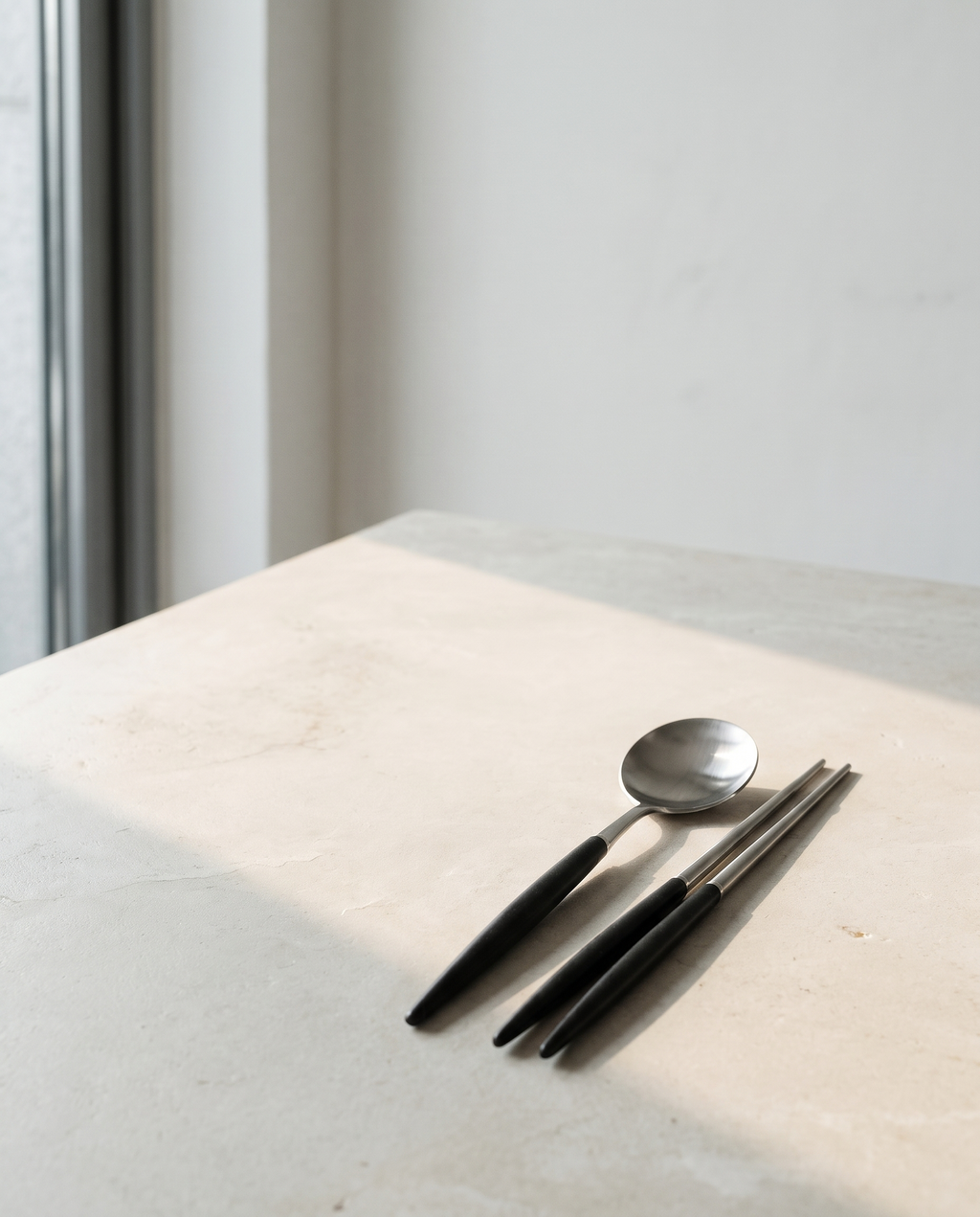 Arc dinner spoon and chopsticks by NR Ceramics, set down at one place on a pale limestone table