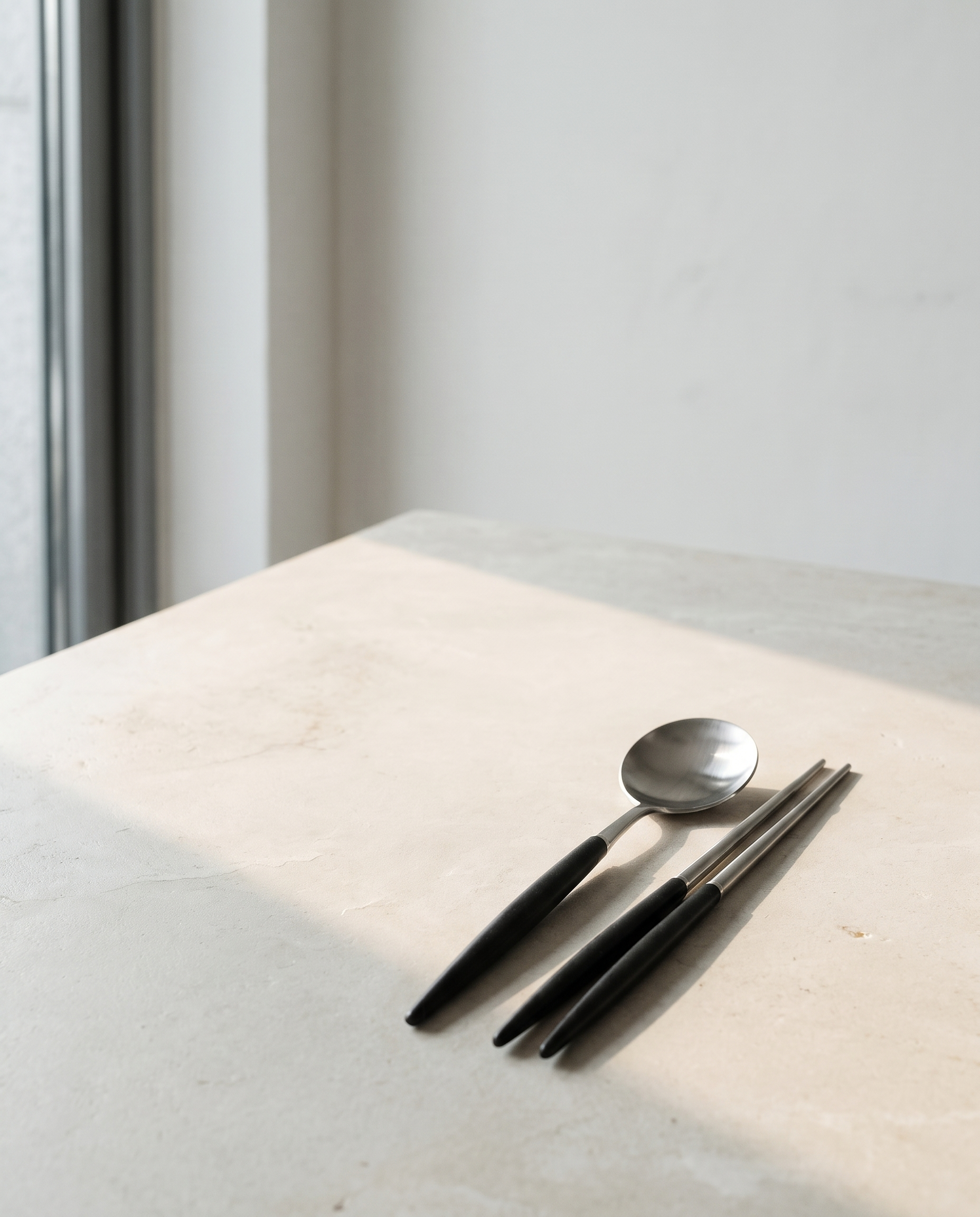 Arc dinner spoon and chopsticks by NR Ceramics, set down at one place on a pale limestone table