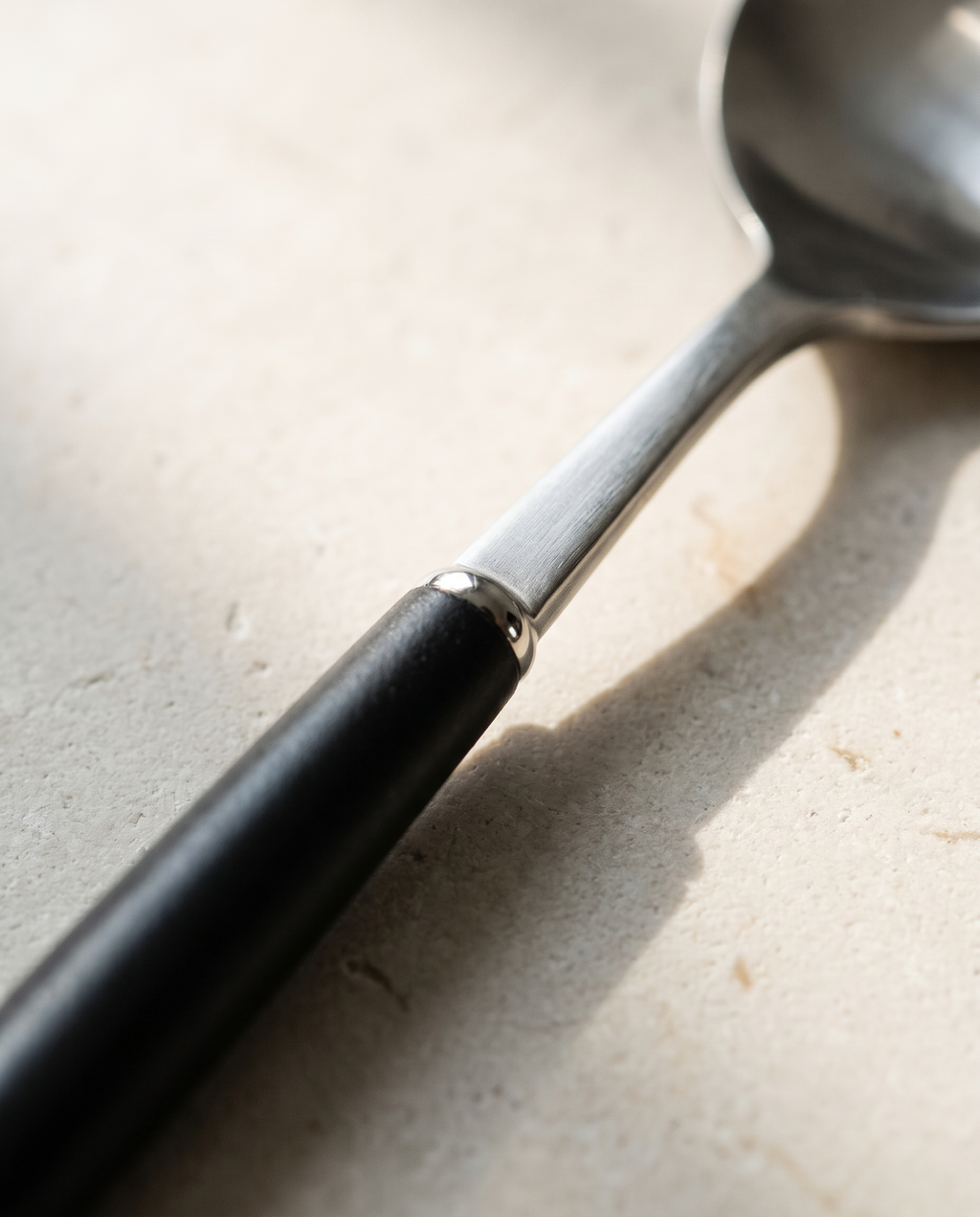 Arc dinner spoon by NR Ceramics, detail of the flat steel shank stepping into the thicker black handle
