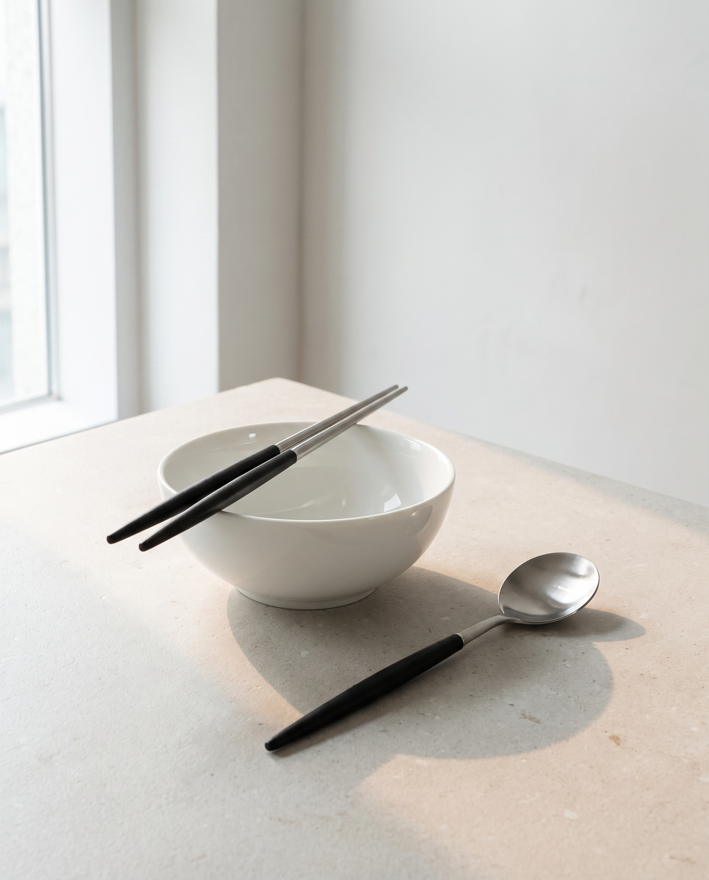 Arc dinner spoon and chopsticks by NR Ceramics, chopsticks resting across the rim of a white porcelain rice bowl