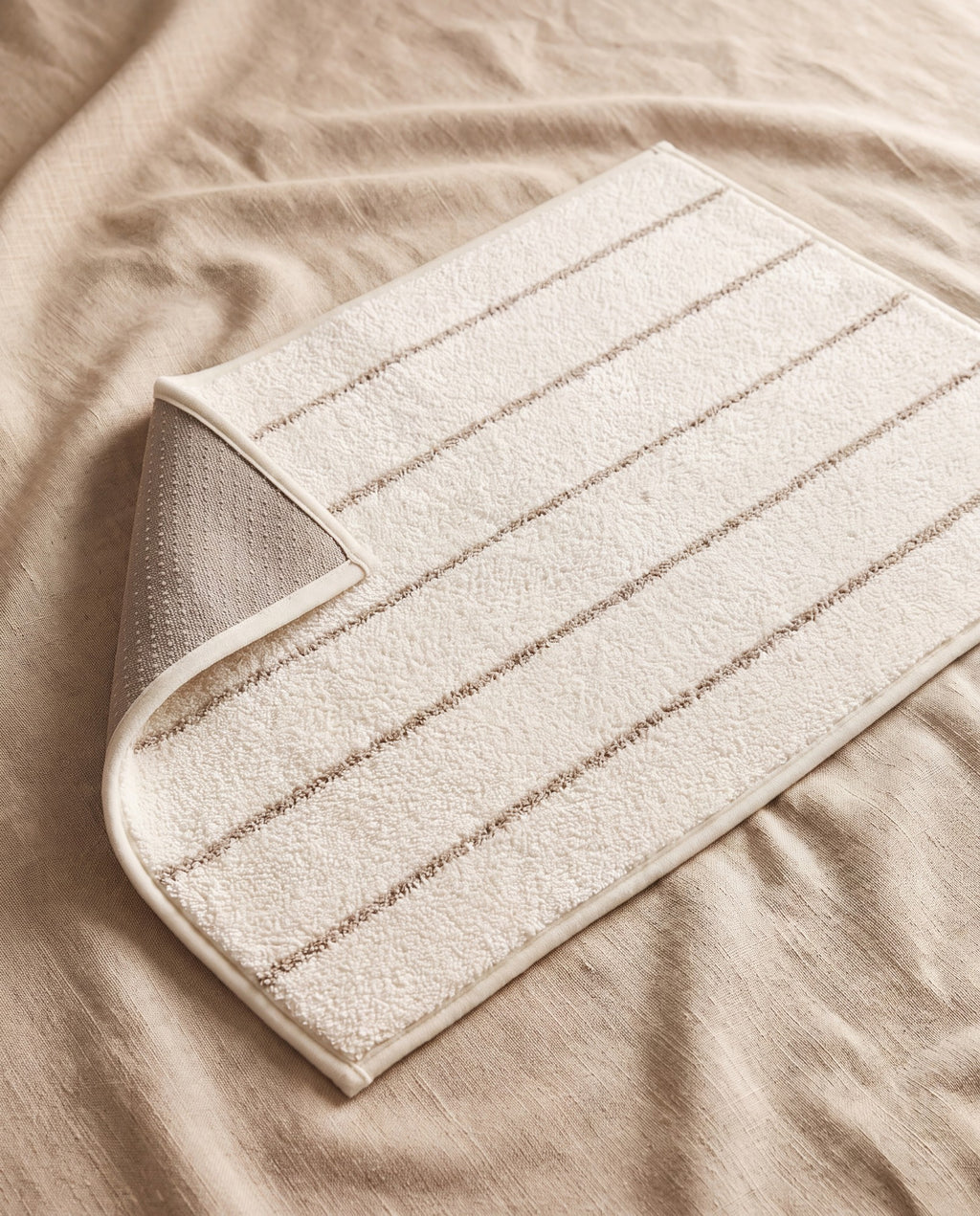 Beige stripe mat in ivory polyester pile with fine taupe stripes, corner turned back to show the non-slip dotted backing