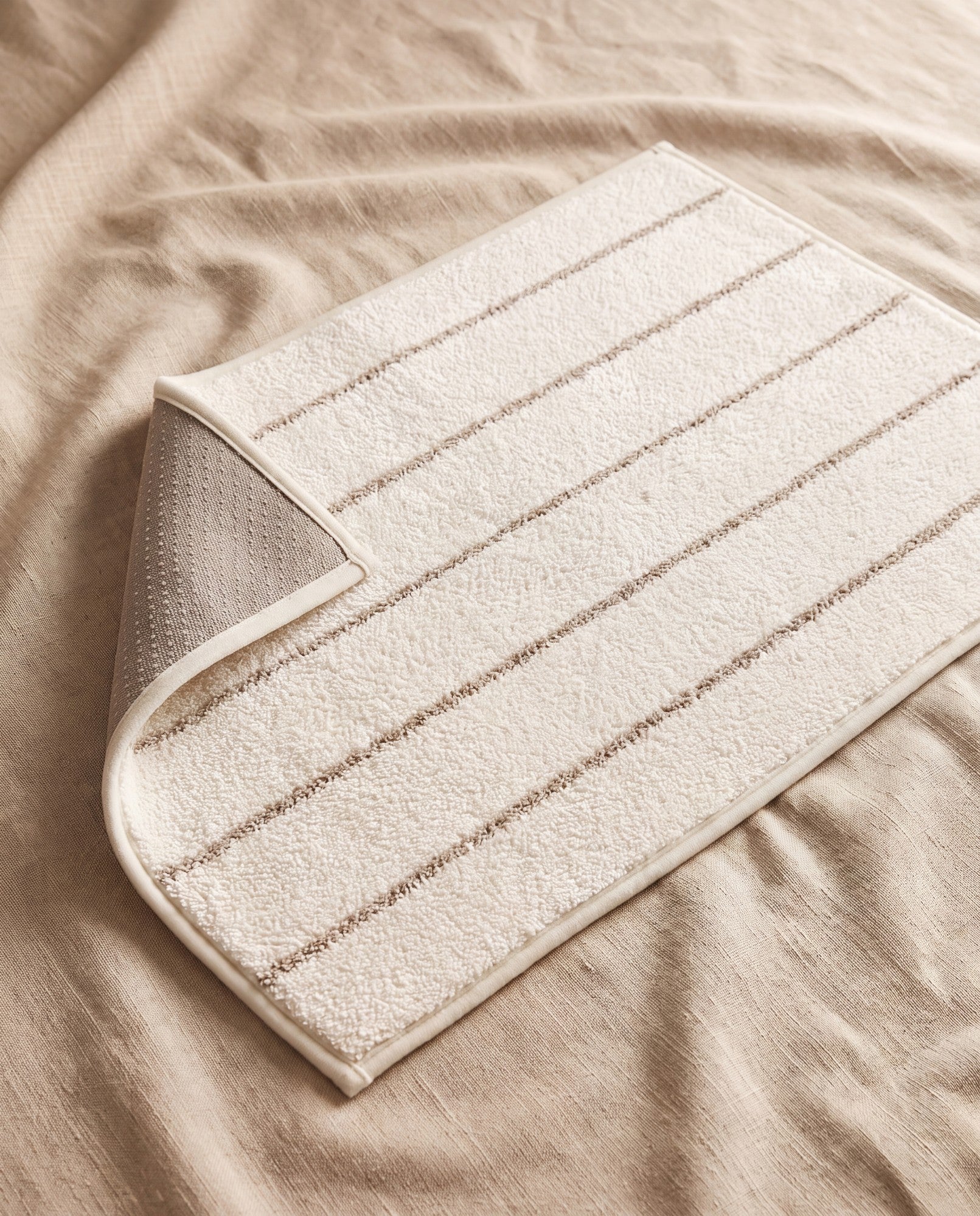 Beige stripe mat in ivory polyester pile with fine taupe stripes, corner turned back to show the non-slip dotted backing