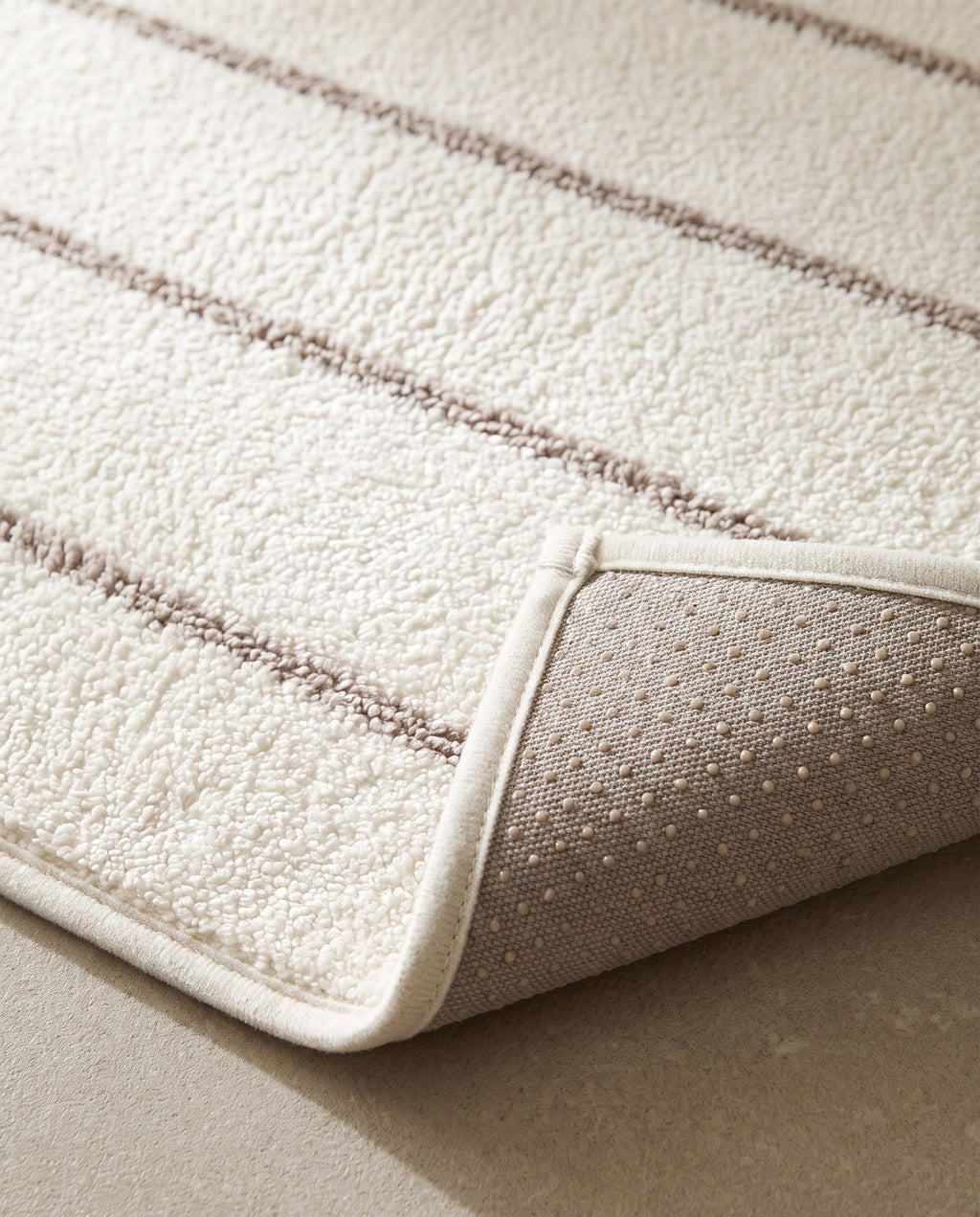 Close-up of the mat pile, taupe stripe and ivory bound edge, with the grey non-slip dotted backing visible