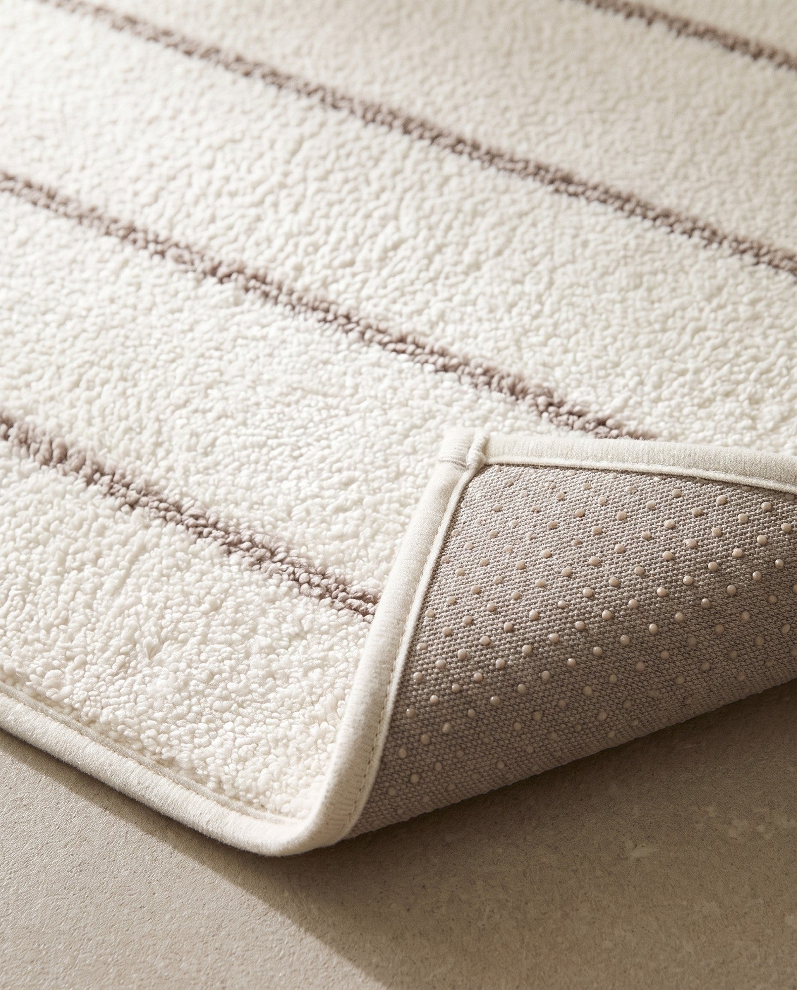 Close-up of the mat pile, taupe stripe and ivory bound edge, with the grey non-slip dotted backing visible