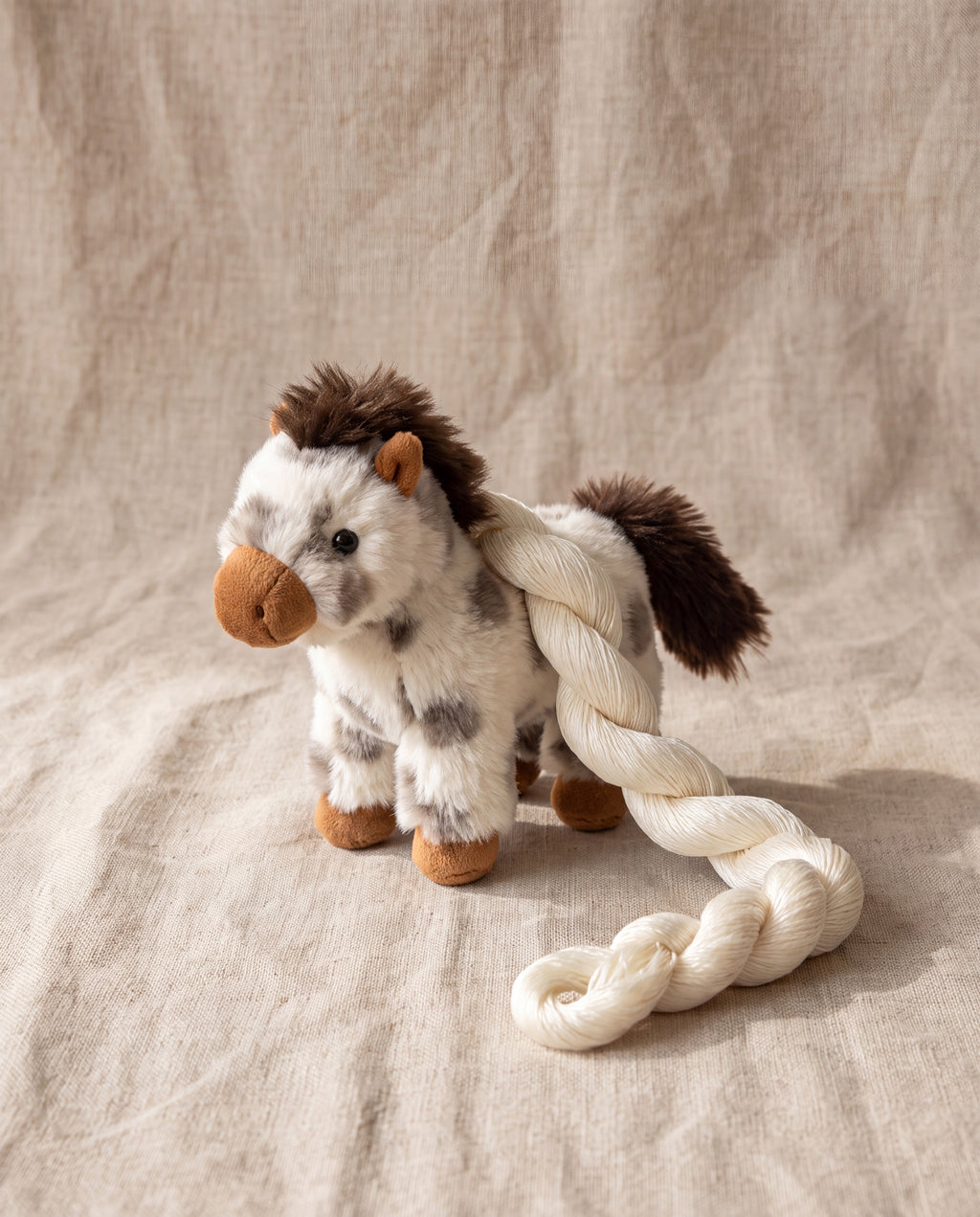 Big Hope pony charm by POUPPET, standing on beige linen with its twisted silk cord