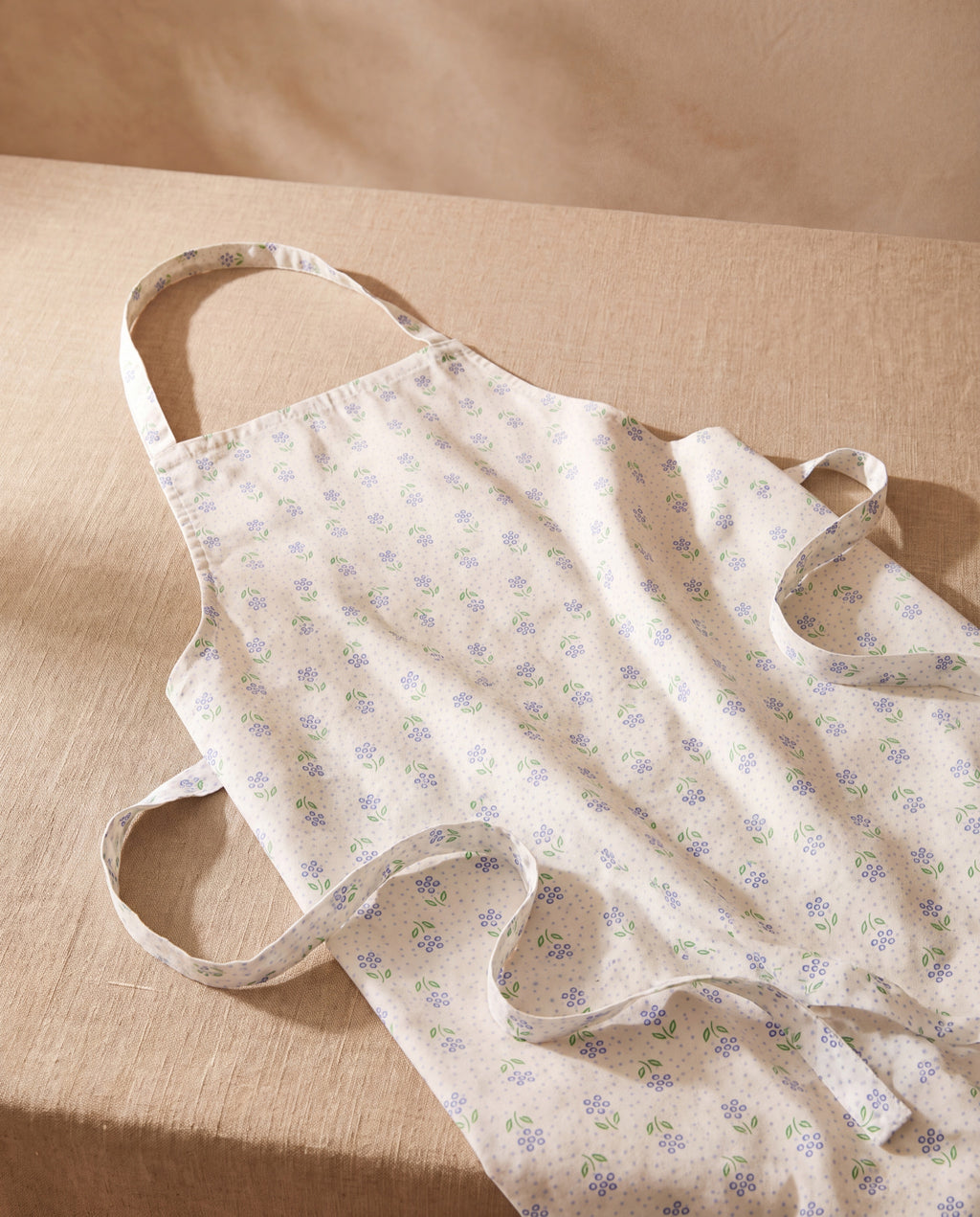 Blair short apron, cream cotton with a small blue floral print, laid on beige linen