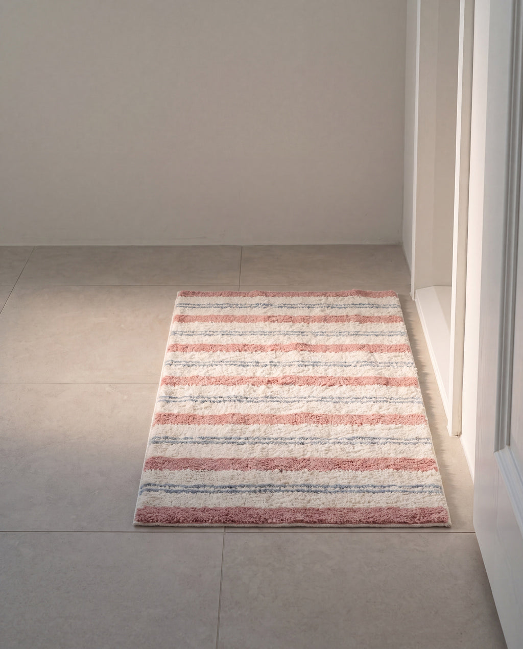 Bold stripe mat by 1401HOME, the bath mat size on pale stone tile at a bathroom doorway