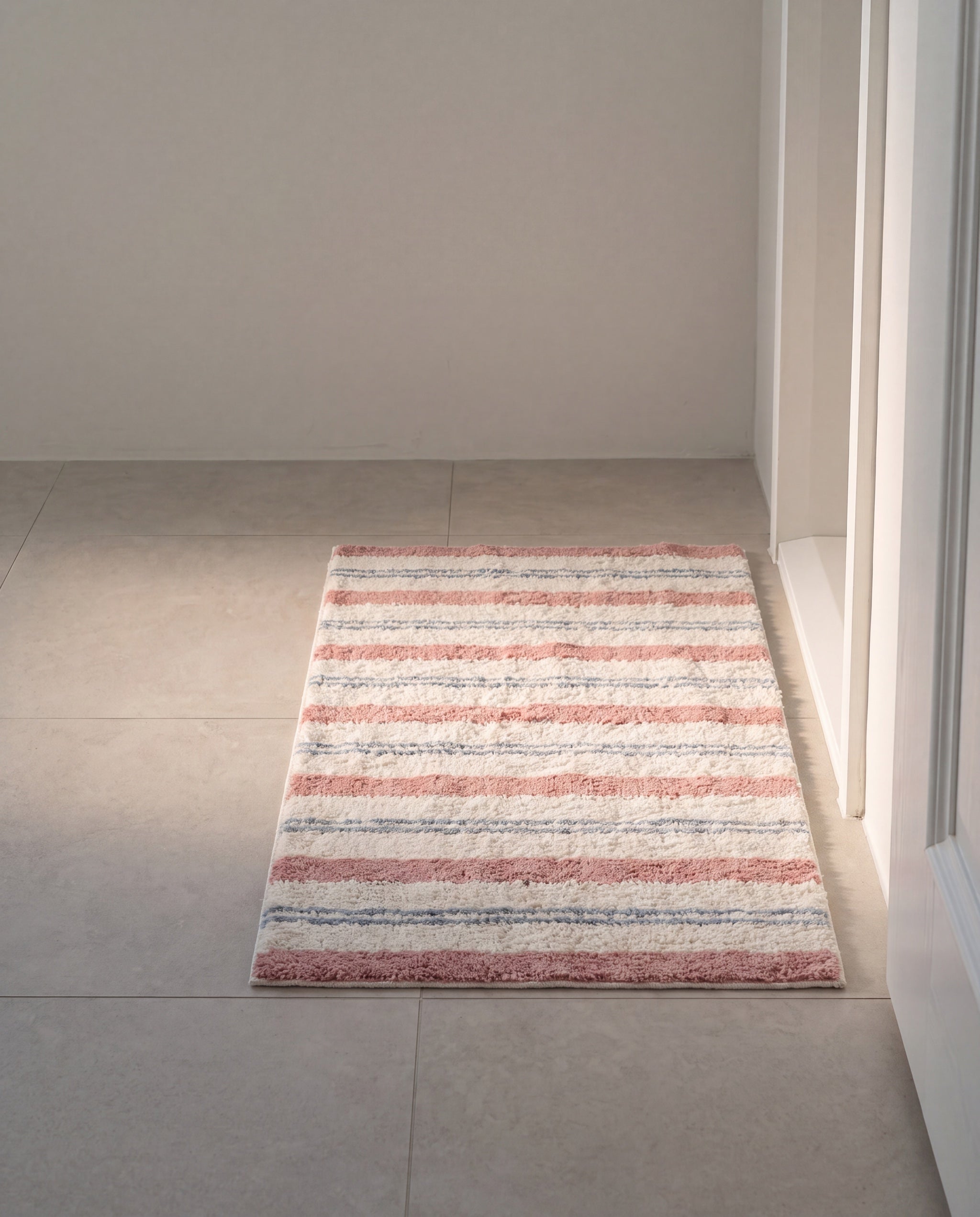 Bold stripe mat by 1401HOME, the bath mat size on pale stone tile at a bathroom doorway
