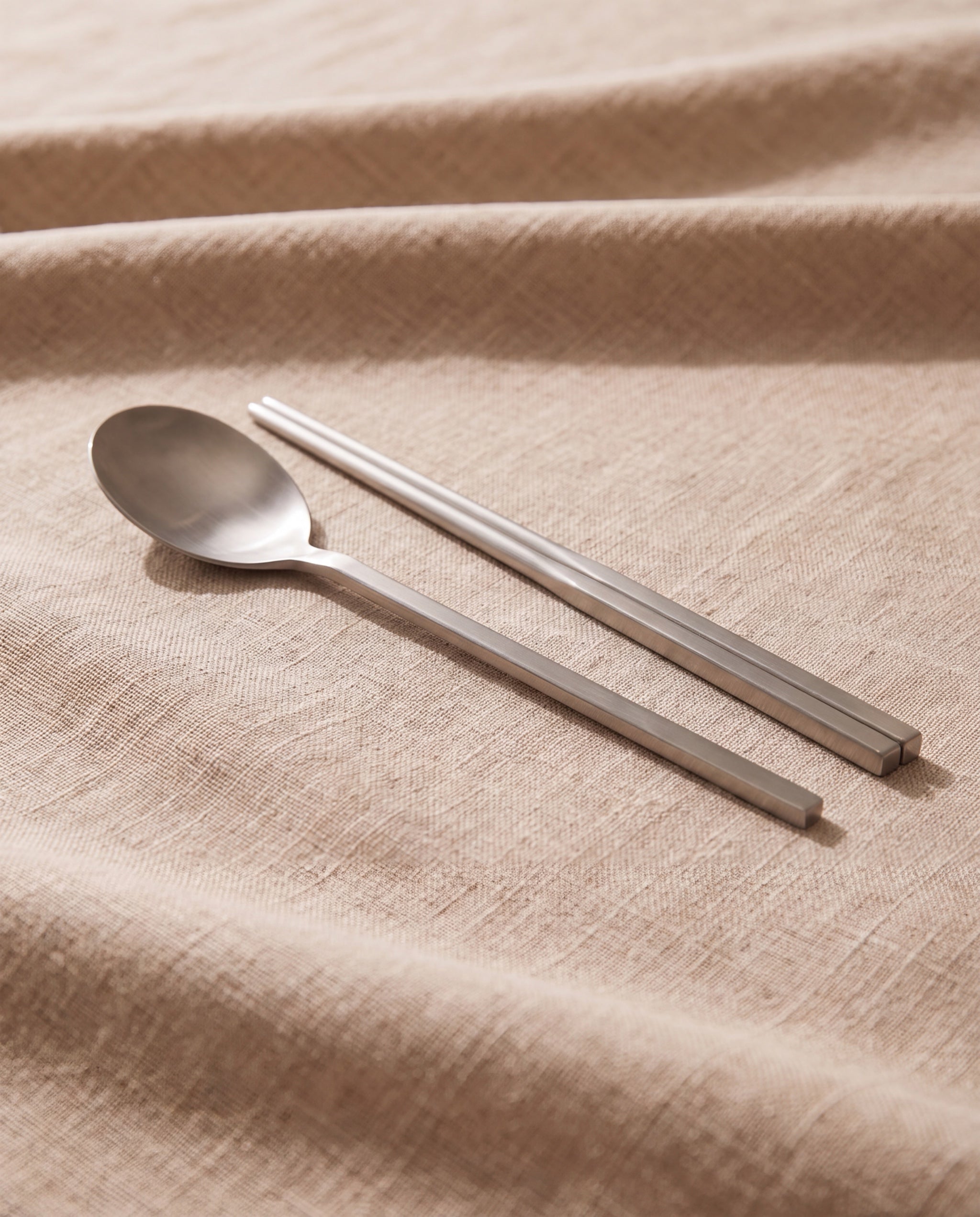 Essential dinner cutlery by NR Ceramics, semi-matte brushed steel on beige linen