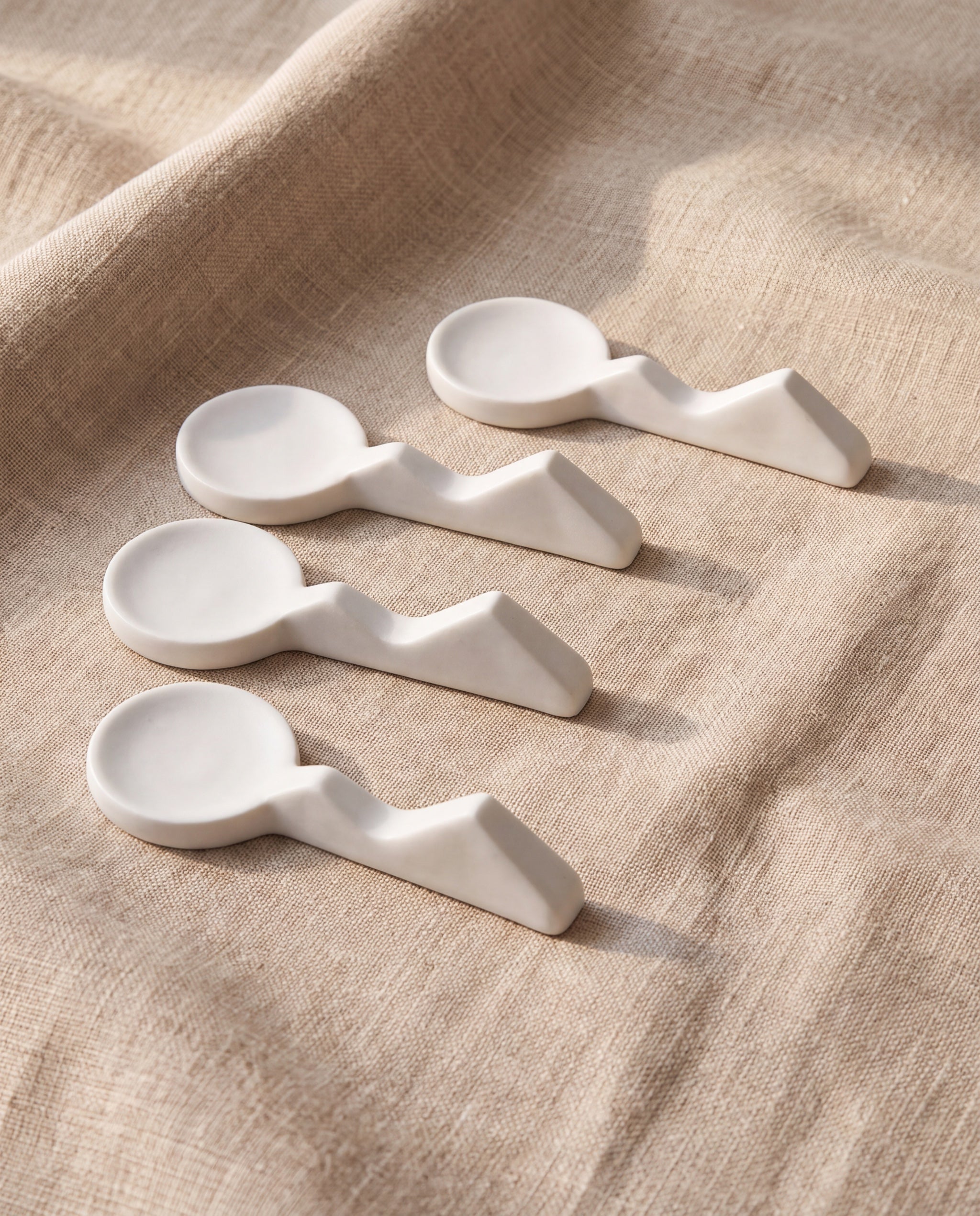 Land scape cutlery rest by Mujagi, four matte white porcelain rests on beige linen