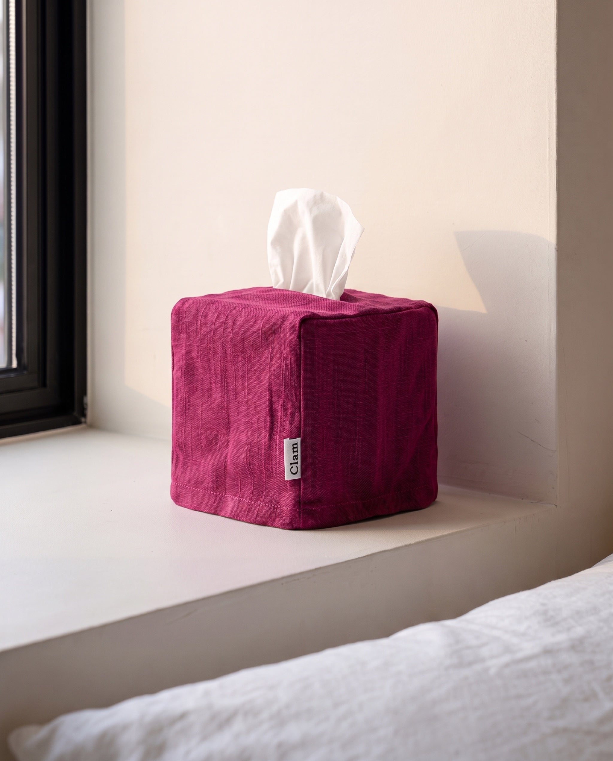 Linen tissue cover by Clam in Plum, a deep magenta linen, on a bedroom window sill
