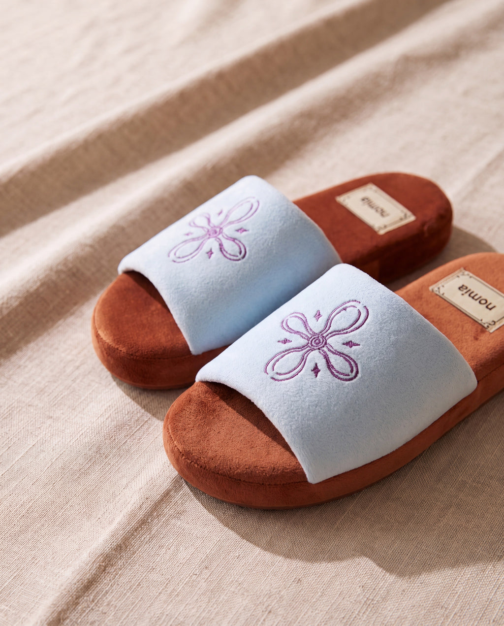 Orchid aqua microfiber room shoes by Nomia, a pair on beige linen