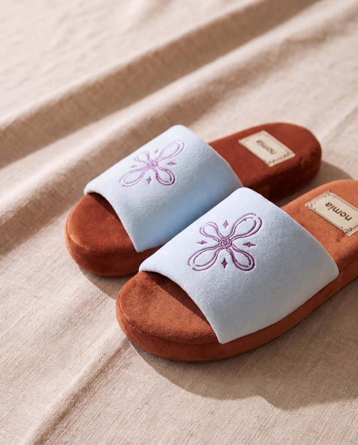Orchid aqua microfiber room shoes by Nomia, a pair on beige linen