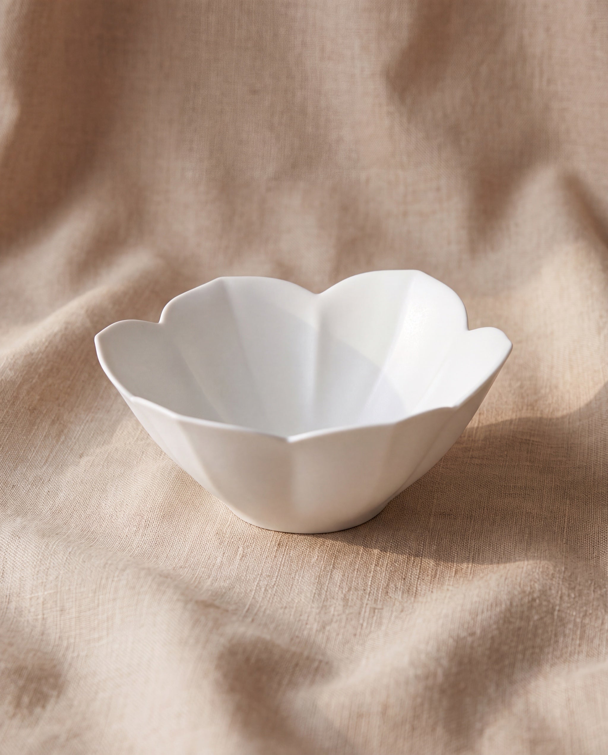 Petal bowl by Mujagi, matte white porcelain on beige linen