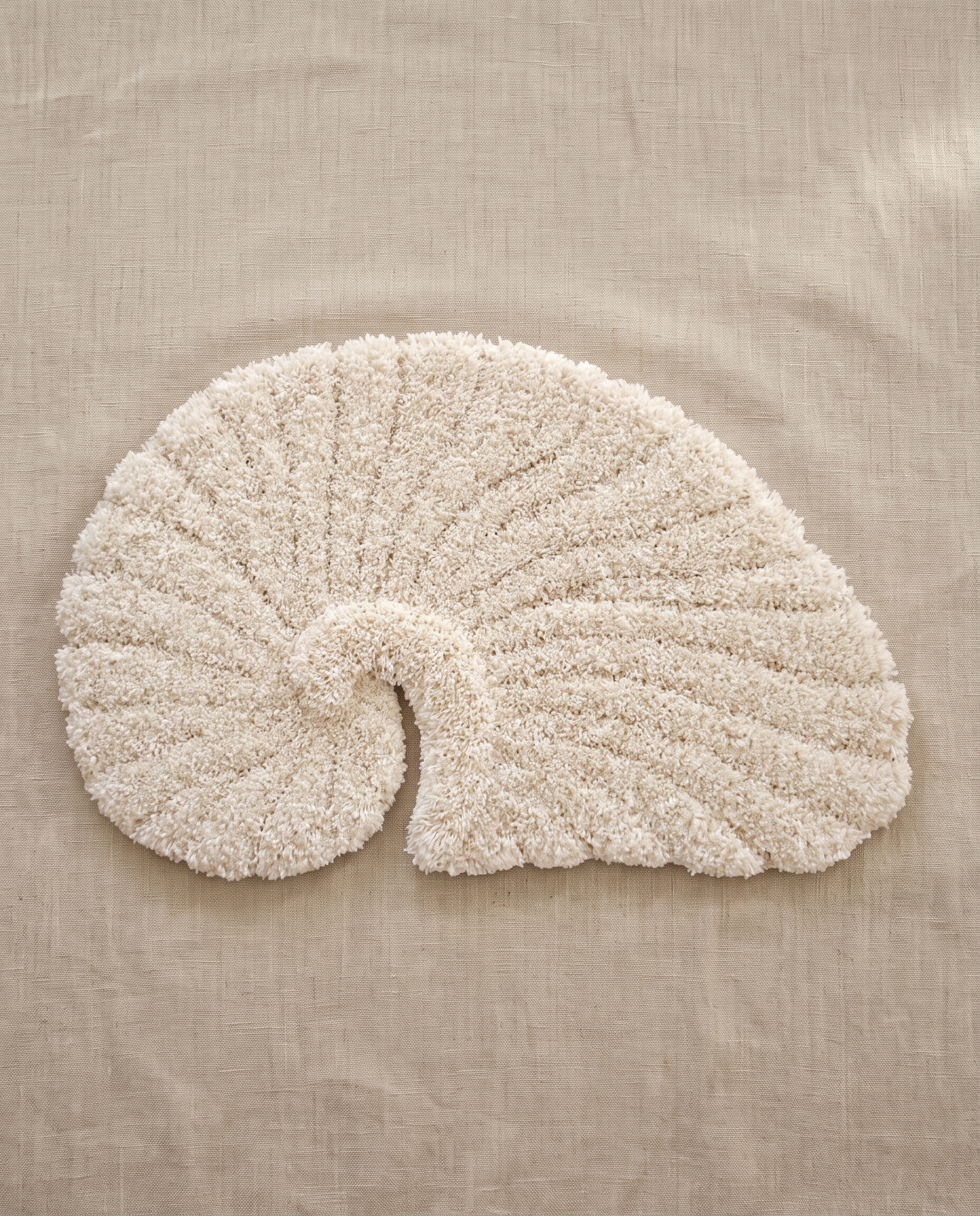 Poh object rug by Lug Lug in beige, a warm ivory nautilus shell tufted in shaggy pile, laid flat on natural linen