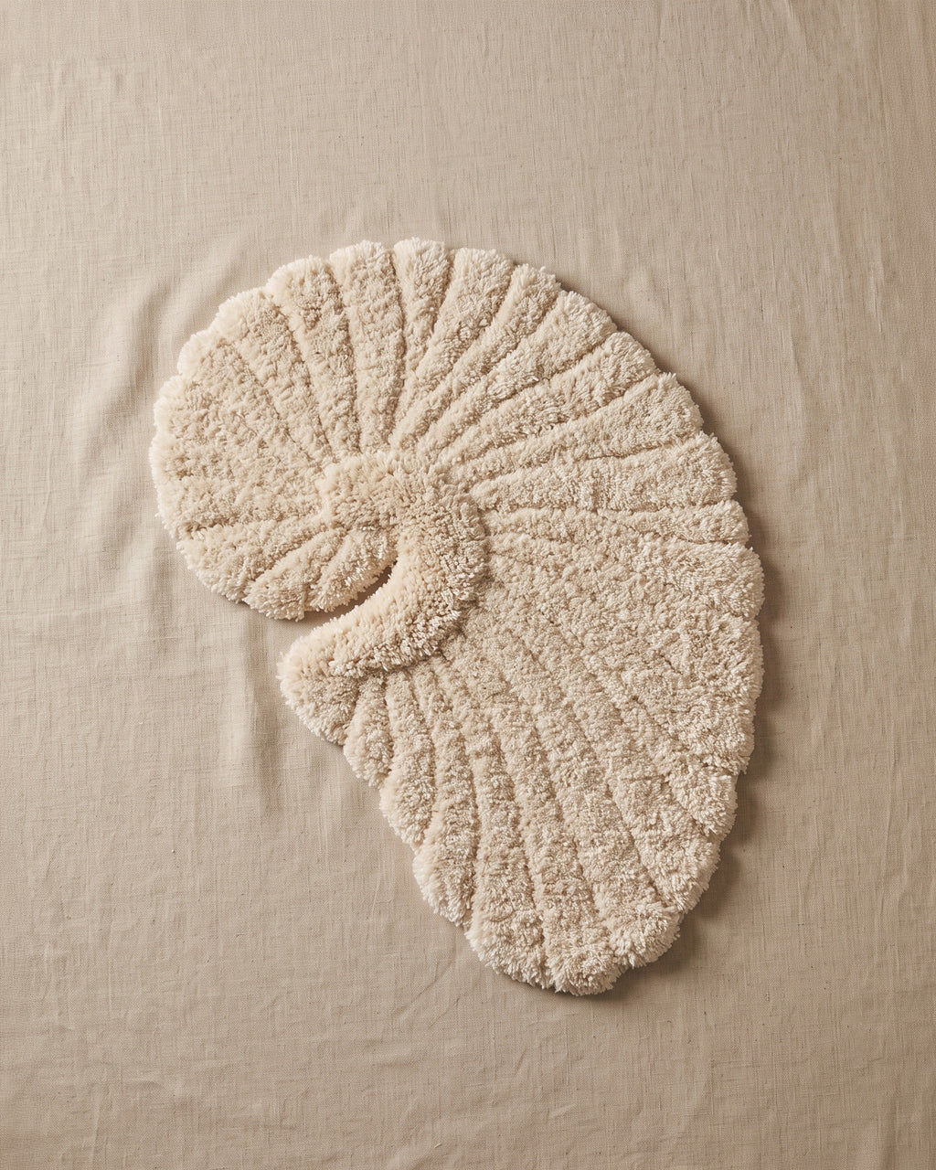 Poh object rug by Lug Lug, the beige colorway seen from above on natural linen, its ribbed shell spiral filling the frame