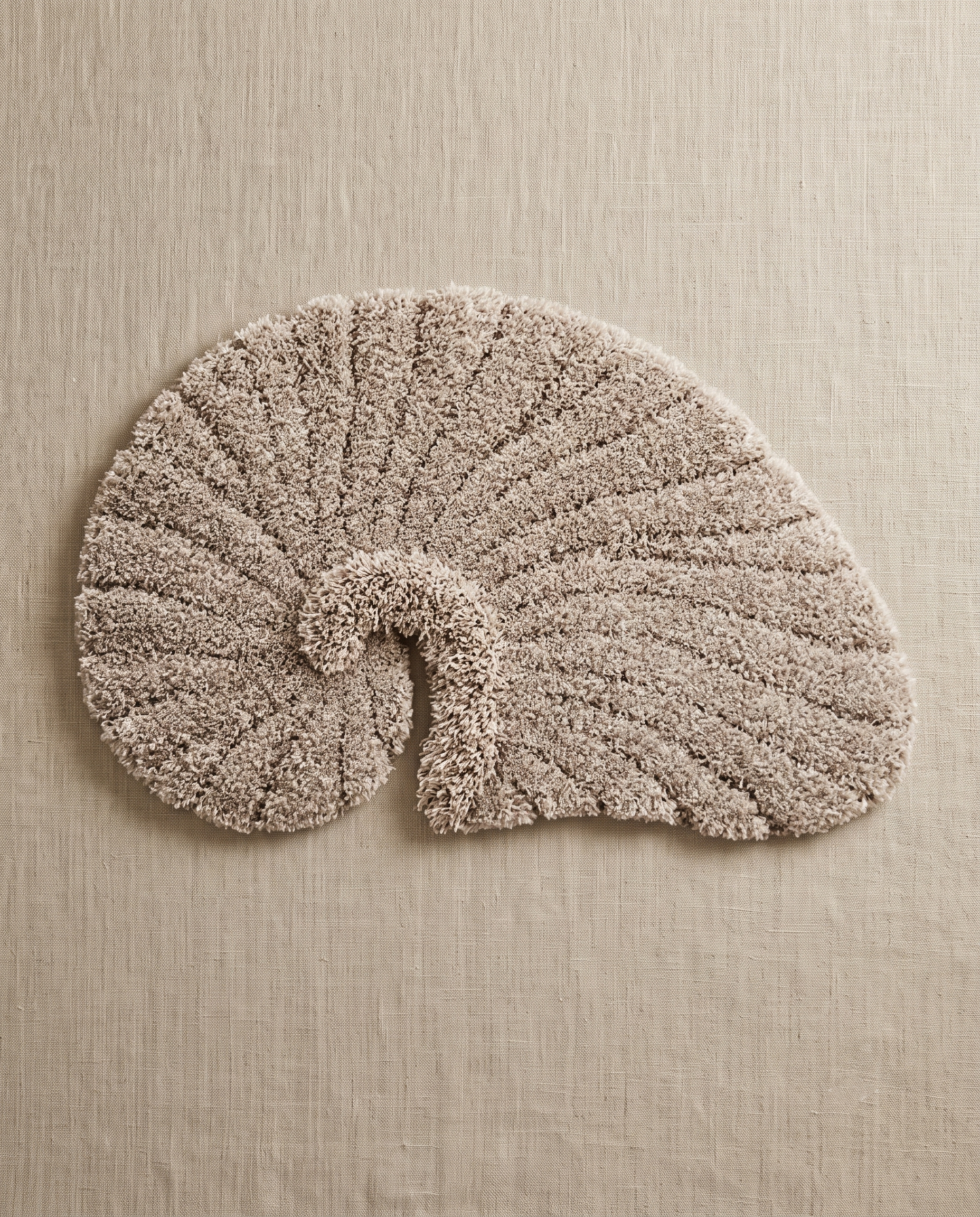 Poh object rug by Lug Lug in gray, a warm greige nautilus shell with the ribbed grooves reading sharply, laid flat on natural linen