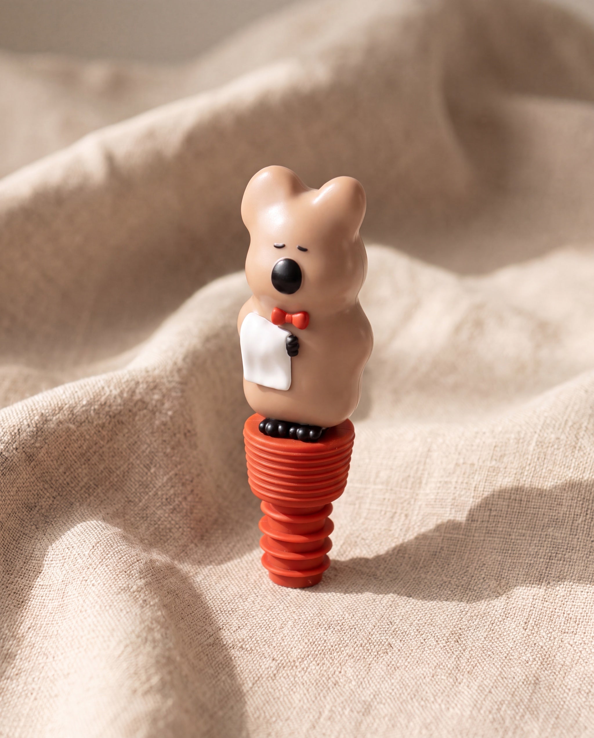 Quokka wine stopper by Dinotaeng, standing on beige linen